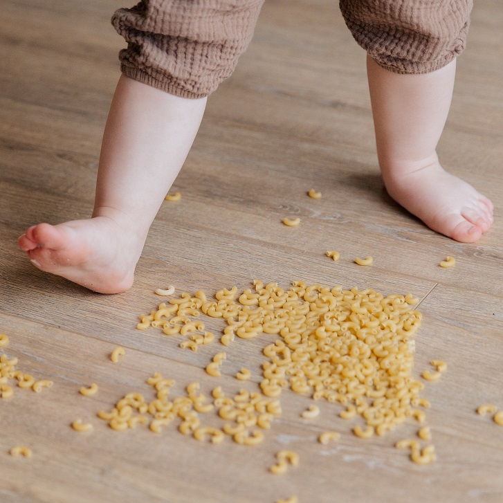Child feet spreading dry pasta on the floor